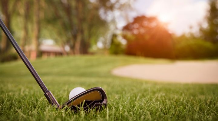 A club about to hit a golf ball in the grass