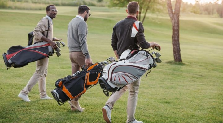 three men carrying clubs in bags walking on the golf course
